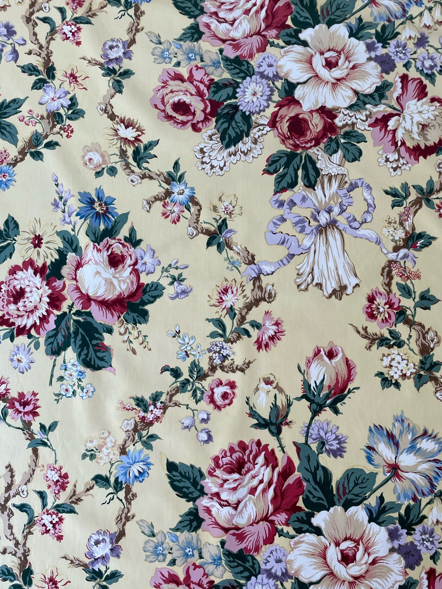 chintz fabric printed with roses, ribbons, and floral vines on a butter yellow background