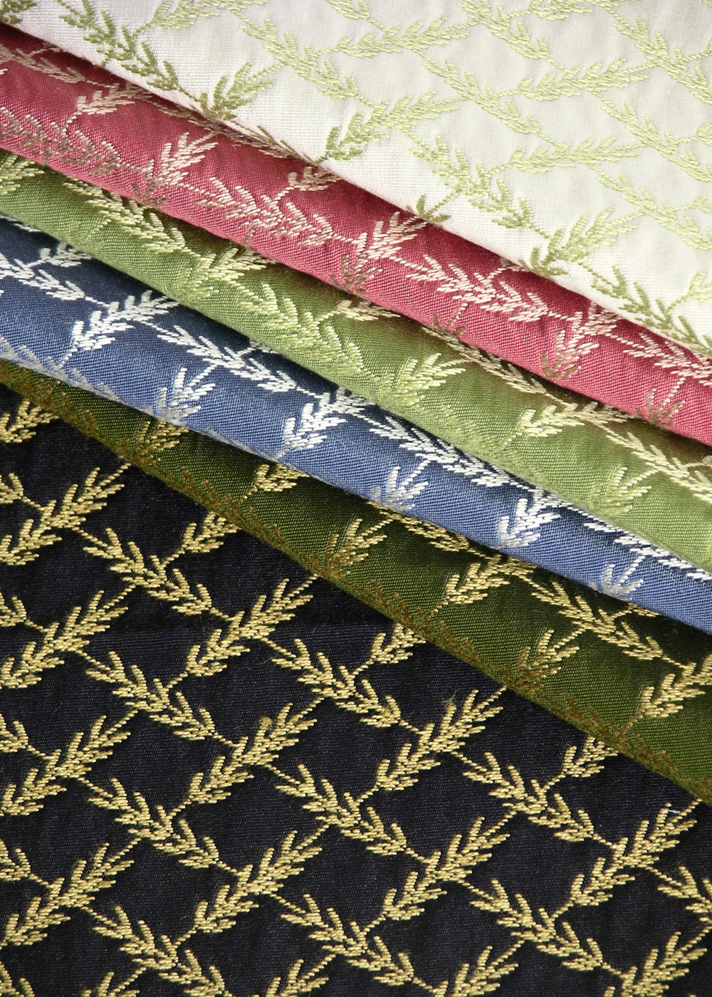 a stack of woven upholstery fabrics that feature a small-scale metallic pattern that looks like ears of wheat